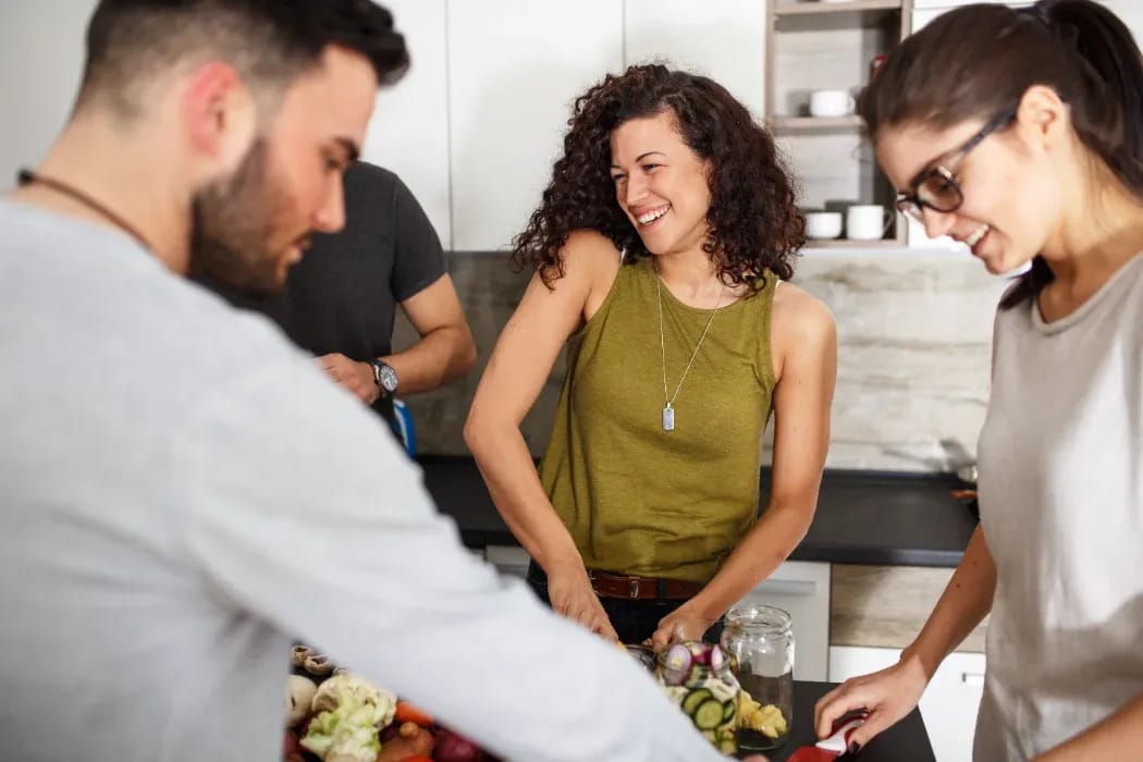 Vier junge Leute schneiden Gemüse und kochen gemeinsam in einer Wohnküche