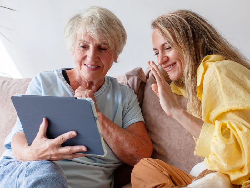 Eine ältere Frau und eine junge Frau sitzen auf dem Sofa und schauen gemeinsam auf ein Tablet